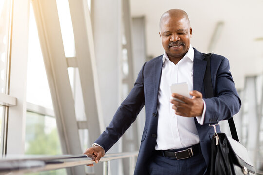 Smiling African American businessman checking smartphone while waiting at airport terminal. Lifestyle concept of global mobility, business travel and communication.