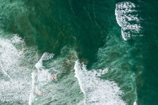 Aerial view of the wild, churning ocean displaying a mesmerizing blend of deep emerald and frothy white near the coast, Princetown, Victoria, Australia.