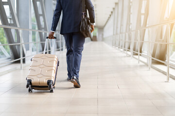 African American businessman in suit walking through airport terminal with rolling luggage. Concept of travel, business trip, mobility and global transportation