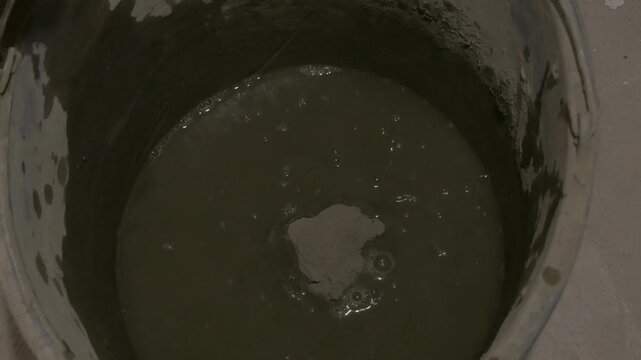 Pouring concrete mixture into water-filled bucket, stirring for optimal consistency and preparation process. pouring concrete mixture into bucked with water 