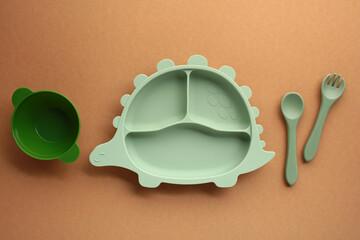 Minimalist flat lay of mint green dinosaur-shaped kids plate with matching utensils and bowl on...