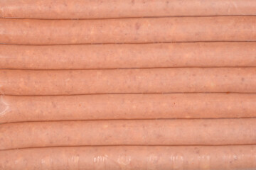 A close-up of several raw beer sausages is shown in a row, still inside their plastic packaging