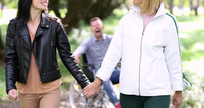 Man in wheelchair screams with frustration while women friends walk away holding hands. Mouth opens wide expressing pain and helpless disappointment