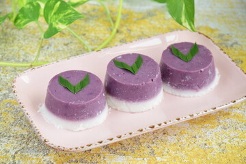 
Indonesian traditional cake Kue Talam Ubi Ungu served on a plate. It is made of a rice flour, coconut milk and other ingredients, garnish with pandan leaves. Indonesian dessert