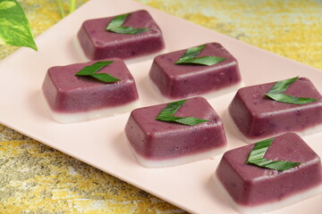 
Indonesian traditional cake Kue Talam Ubi Ungu served on a plate. It is made of a rice flour, coconut milk and other ingredients, garnish with pandan leaves. Indonesian dessert