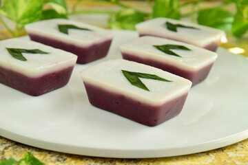 
Indonesian traditional cake Kue Talam Ubi Ungu served on a plate. It is made of a rice flour, coconut milk and other ingredients, garnish with pandan leaves. Indonesian dessert
