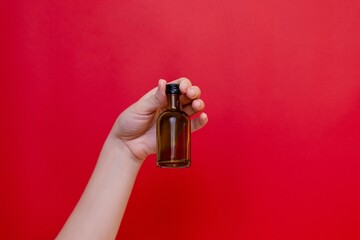 Elegant hand with small glass blank bottle mockup on red background. Package for cosmetics product,...