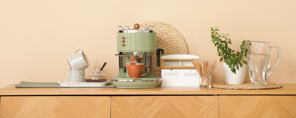 Modern coffee machine with cups, houseplant and bowl of beans on counter in kitchen