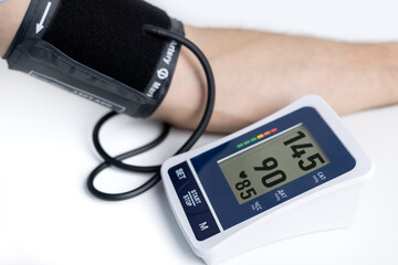 Hands with a tonometer on the table. Man in a shirt measures blood pressure with an electronic tonometer
