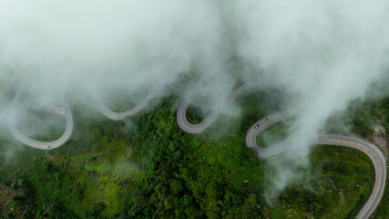 curvy road and winding path and small car driving, clouds and fog on top on the mountain up to Phu...