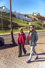 Senior mother and adult daughter walking together on the seafront promenade in Tangier, Morocco,...