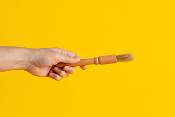 Hand using a wood little paintbrush isolated on a yellow background