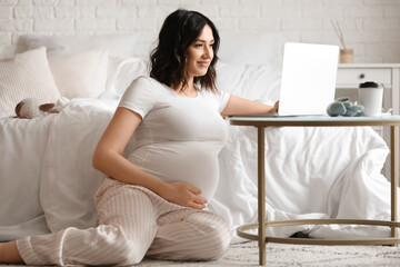 Young pregnant woman working with laptop in bedroom