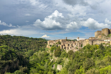 Fototapeta premium panoramic view of a historic hilltop village surrounded by lush green cliffs under a cloudy sky