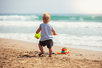 A small baby boy walks along the beach on a sunny summer day