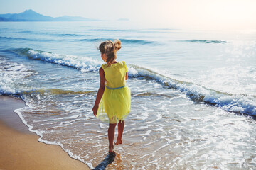 Activity on the beach in summer. Happy little girl runs on the beach. The kid in the yellow dress.