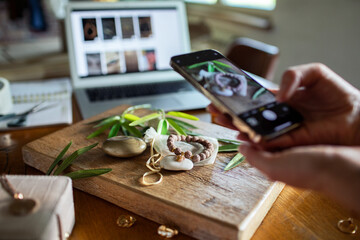 Woman photographing handmade jewelry products for online shop at home