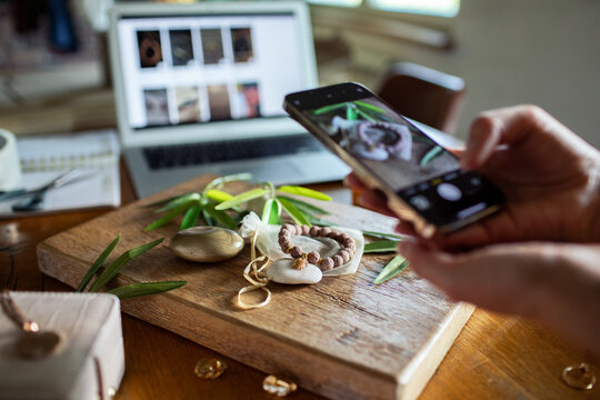 Woman photographing handmade jewelry products for online shop at home