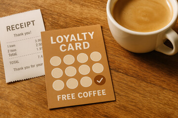Loyalty card with stamp for free coffee next to receipt and cup of coffee on wooden table