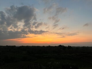 Vibrant orange sunset with dramatic clouds over rural fields and distant hills, scenic evening sky in countryside.