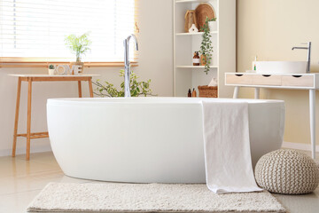 Bathtub with towel, sink and shelving units in interior of bathroom