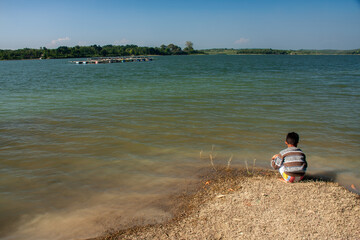 A child is playing by a clear lake with a blue sky background.