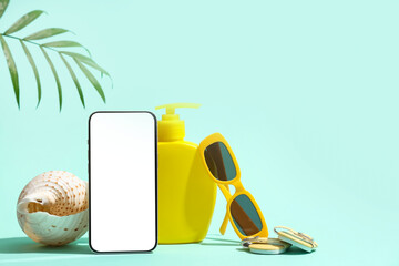 Mobile phone with sunscreen, sunglasses and seashell on turquoise background
