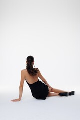 Fototapeta premium Beautiful young woman in a black elegant dress posing in studio on white background. Fashion model with long hair, red lips, and stylish earrings. Glamour portrait, studio photoshoot, beauty 