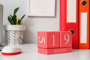 Cube calendar with date August 19, PC mouse, folders and houseplant on light table