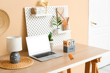 Obraz premium Stylish workplace with modern laptop, cube calendars and pegboard near color wall