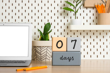 Cube calendar, modern laptop and pencils on table against pegboard