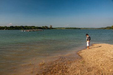 A child is playing by a clear lake with a blue sky background.