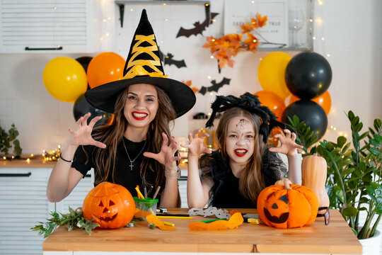 A happy family is getting ready for Halloween. Mother and child daughter in carnival costumes at home in the kitchen having fun scaring each other and laughing
