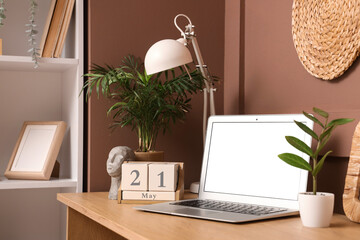 Modern laptop, cube calendar with date 21 May, lamp and houseplants on wooden table