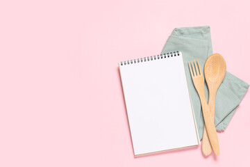 Blank recipe book, napkin and wooden cutlery on pink background