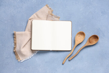 Blank recipe book, wooden spoons and napkin on color background