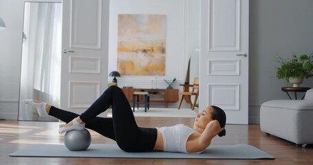 Woman performing fitness exercise with stability ball in modern living room environment - Powered by Adobe