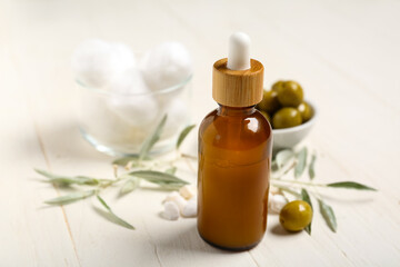 Bottle of natural essential oil, cotton balls and green olives on light wooden background