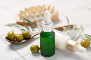 Bottles of natural essential oil, massage brush and green olives on light tile background