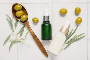 Composition with bottles of natural essential oil, green olives and branches on light tile background