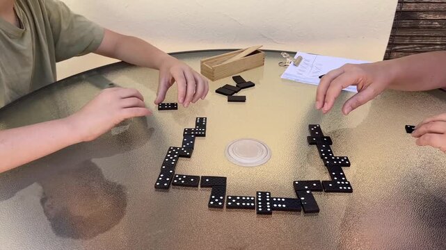 Handshake between mother and her 12-year-old son after a game of dominoes on a round glass table, symbolizing respect, agreement and family bonding in a peaceful outdoor setting