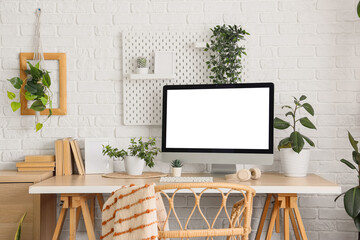Workplace with blank computer monitor and green plants near white brick wall in office