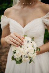 The bride in a white dress with a large neckline and a necklace around her neck holds a bouquet of...