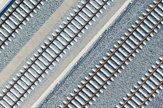 Aerial view of parallel railway tracks cutting through the gravel landscape, their metallic sheen glinting under the sun, Koralmbahn, Deutschlandsberg, Steiermark, Austria.