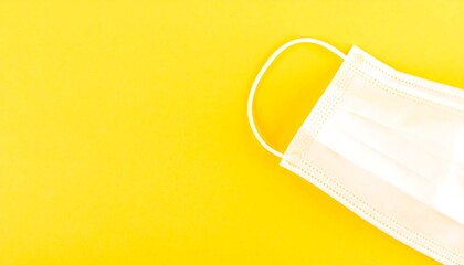 A single, white disposable face mask lies diagonally on a vibrant yellow background.