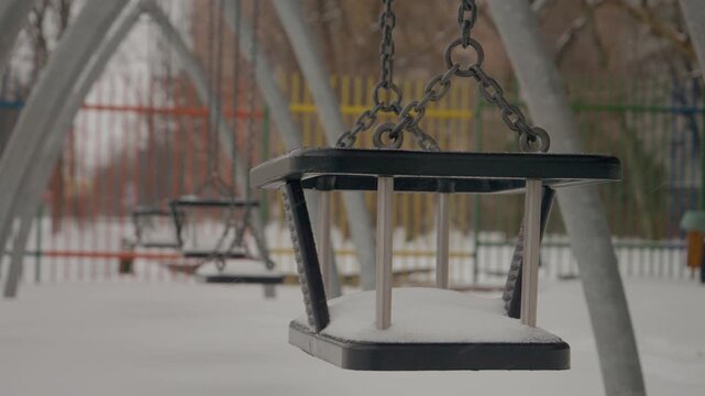 Snow gently blankets the urban playground, transforming swings and slides into winter wonders. Children will enjoy this magical scene once the snowfall stops.