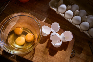 overhead kitchen view showing a wooden counter with a bowl of yolks and whites, scattered...