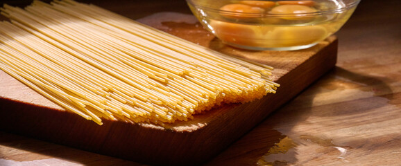 Golden egg spaghetti shines under warm sunlight in a rustic Italian kitchen. Next to the pasta, a...