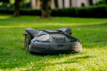 Robot lawnmower cutting grass in backyard, innovative gardening technology, smart landscaping tool, eco electric mower for garden maintenance, quiet automatic lawn care machine in summer park