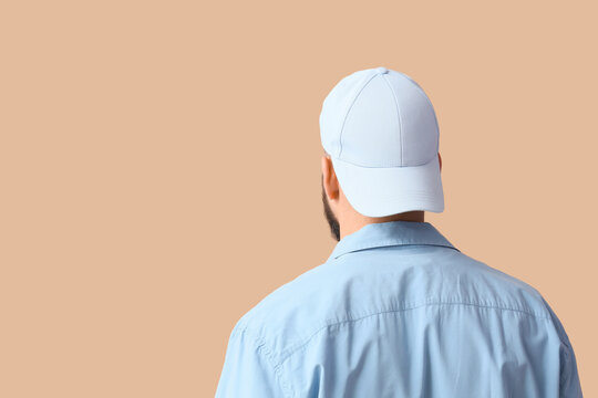 Handsome young man in stylish cap on beige background, back view